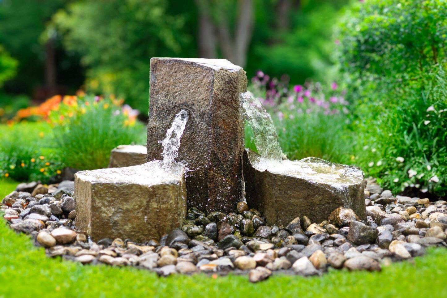 4-stone basalt fountain kit with three cascading streams and 360-degree center column in landscaped garden setting