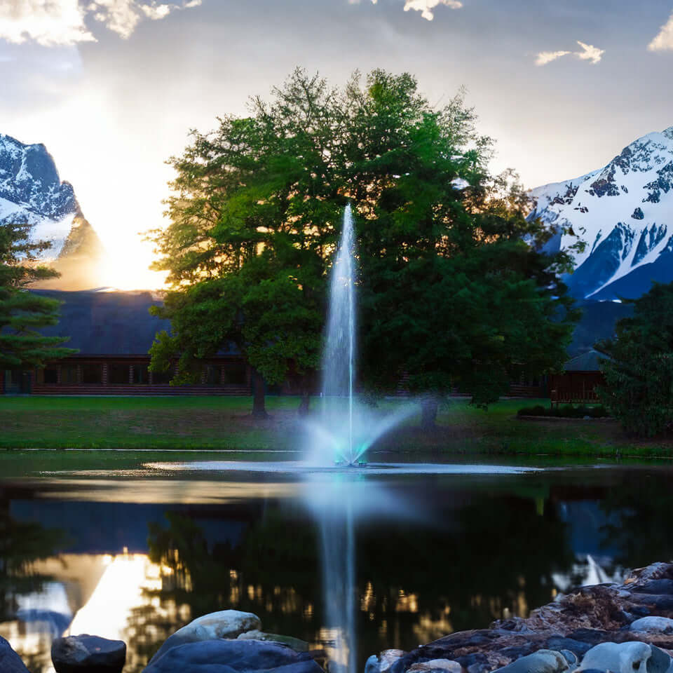 Scott Aerator Skyward pond fountain spraying tall water plume in a lakeside pond at sunset with mountains in the background