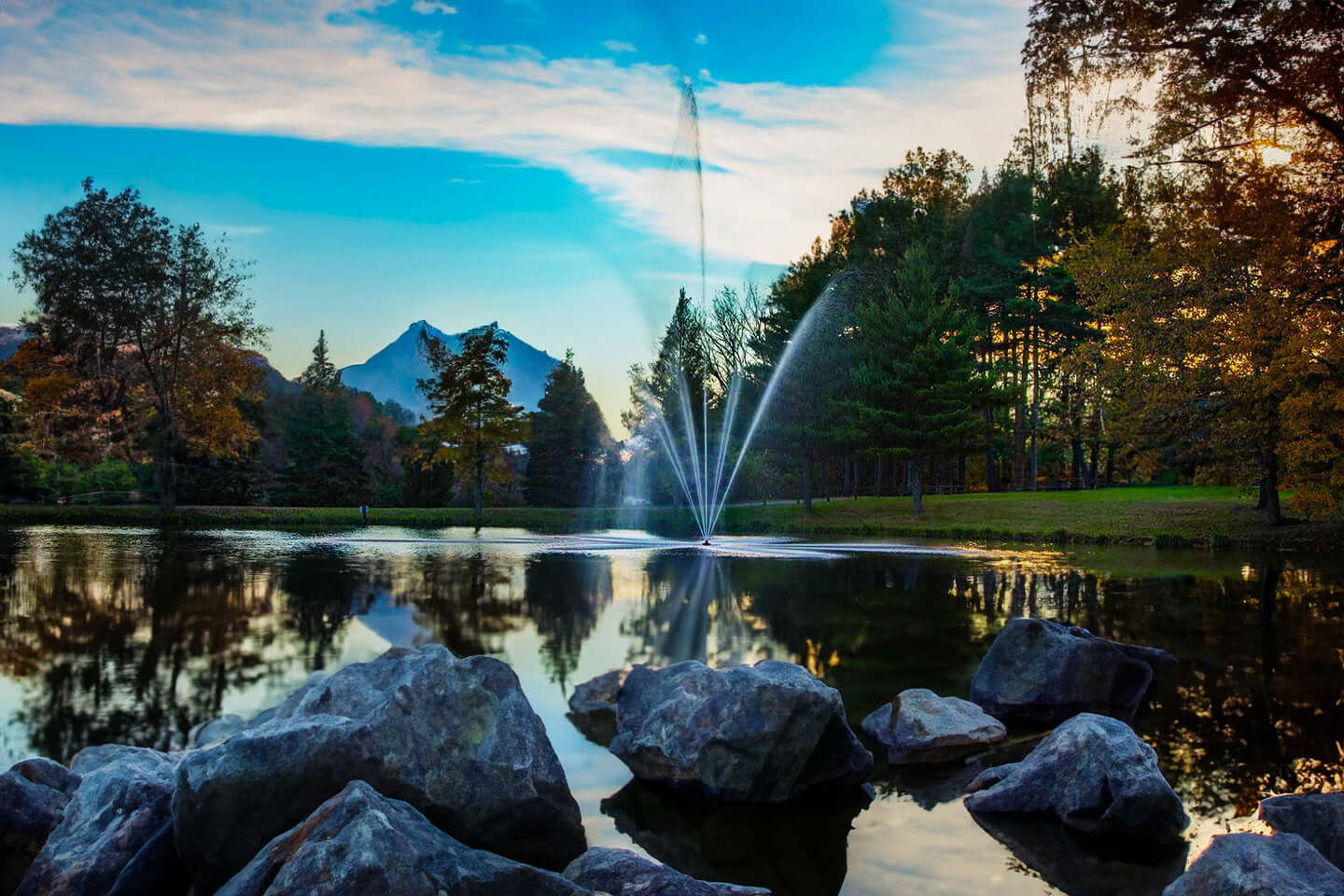 Scott Aerator Atriarch pond fountain spraying water in a landscaped pond with rocks, trees, and mountain view