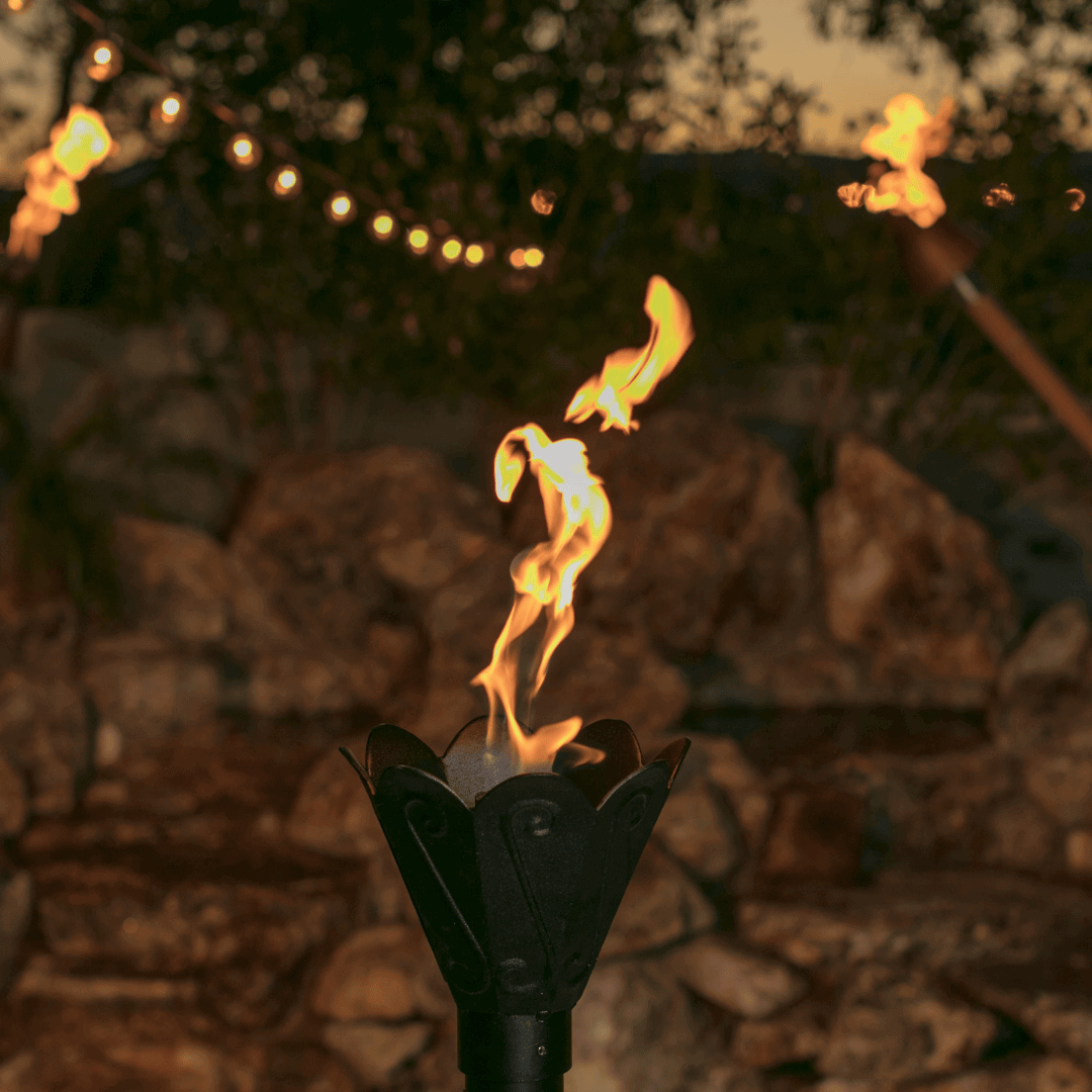Tulip automated ignition tiki torch burning at dusk, outdoor patio ambiance with warm flame and string lights