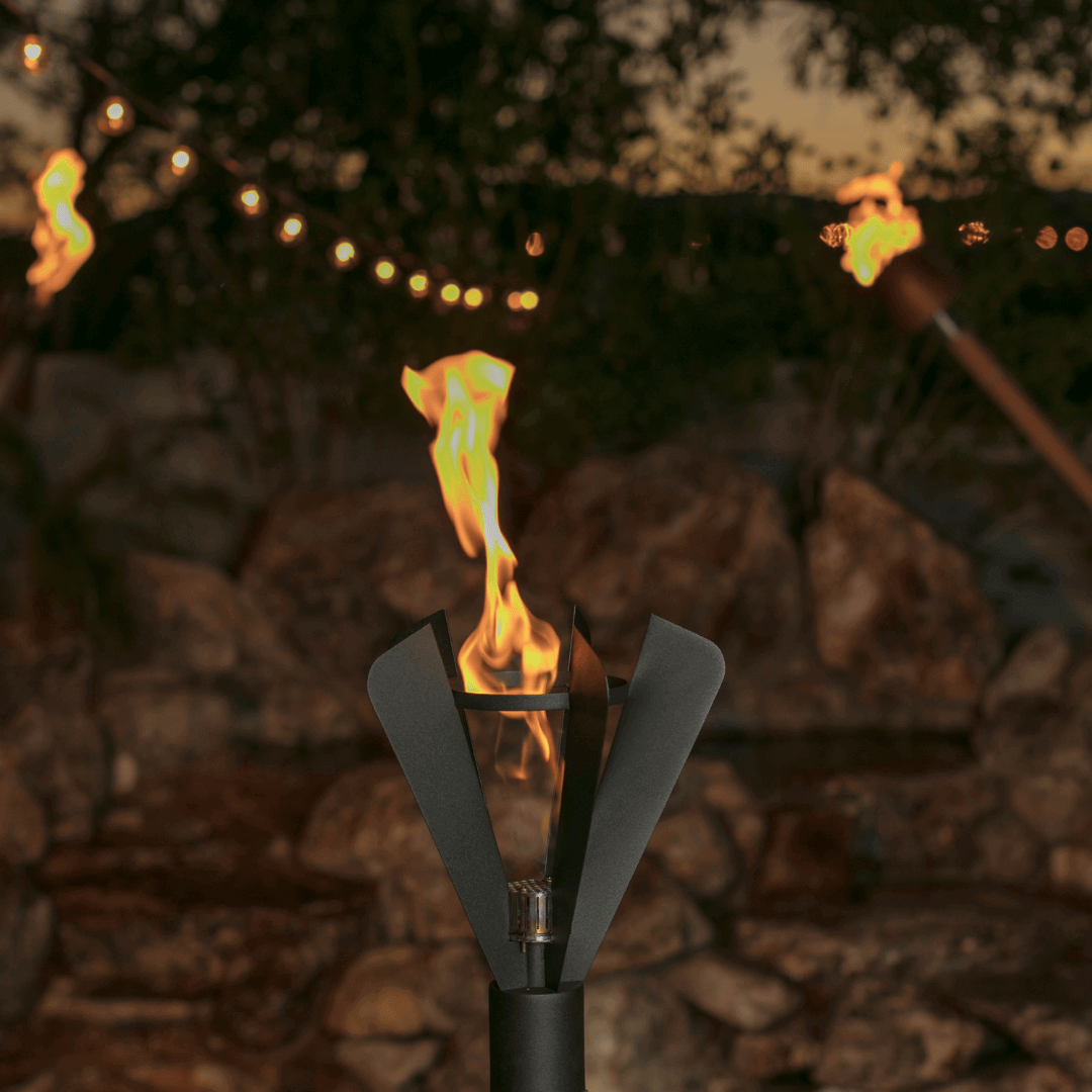 auto ignition fin style tiki torch lit at night with tall flame, outdoor patio ambiance with string lights