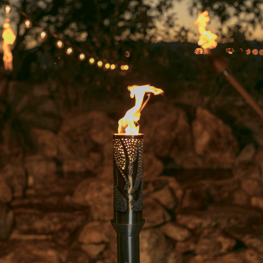 bird of paradise automated tiki torch lit at dusk, decorative metal flame torch with outdoor string lights and stone backdrop