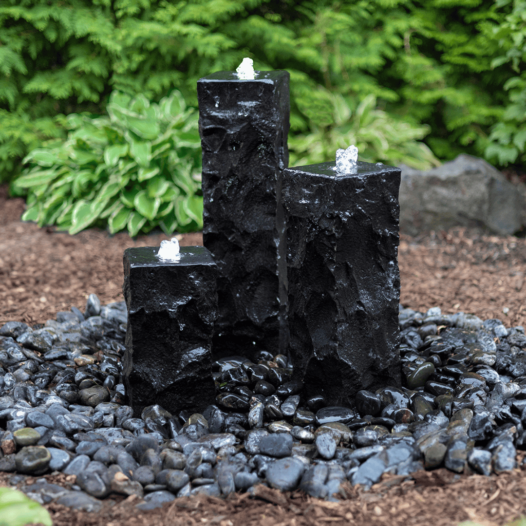 Ebony Basalt Fountain Complete Kit with three bubbling basalt columns on black river rocks outdoors - ebony basalt fountain kit