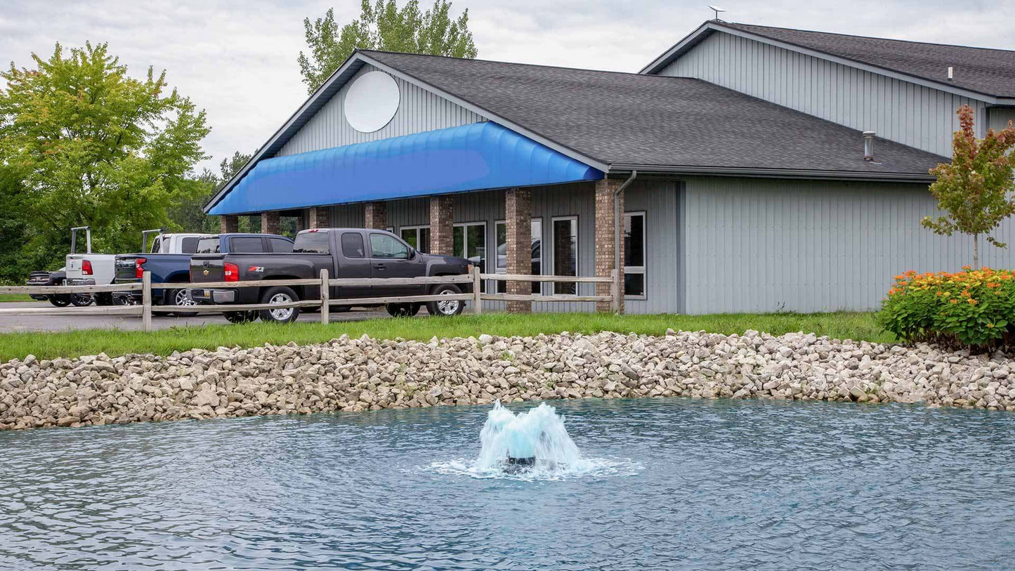 solar powered pond aerator circulating water in front of lakeside building with blue awning and parked trucks