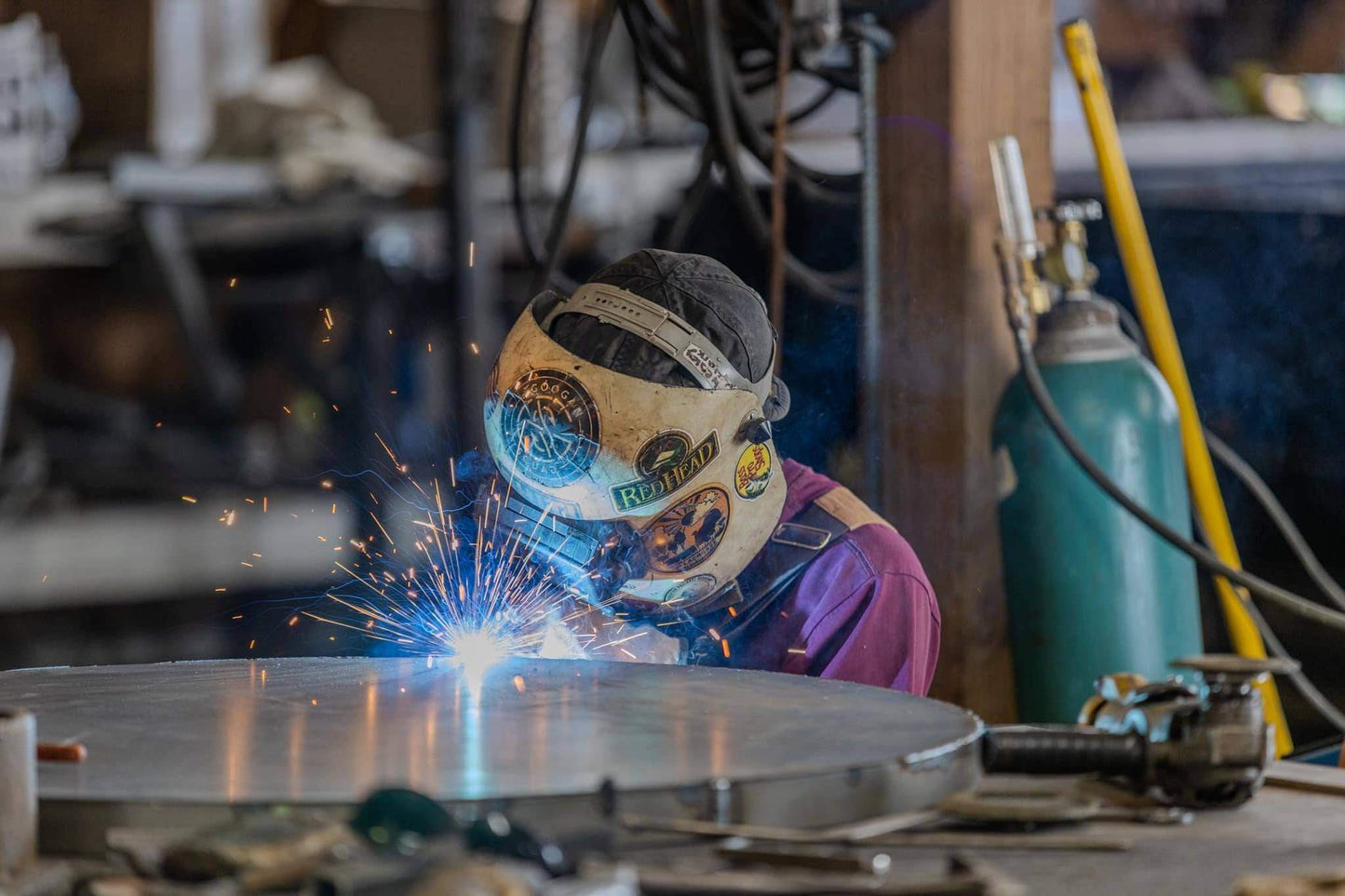 37 inch steel fire pit with footrest being handcrafted in USA workshop as welder fabricates thick carbon steel fire pit bowl