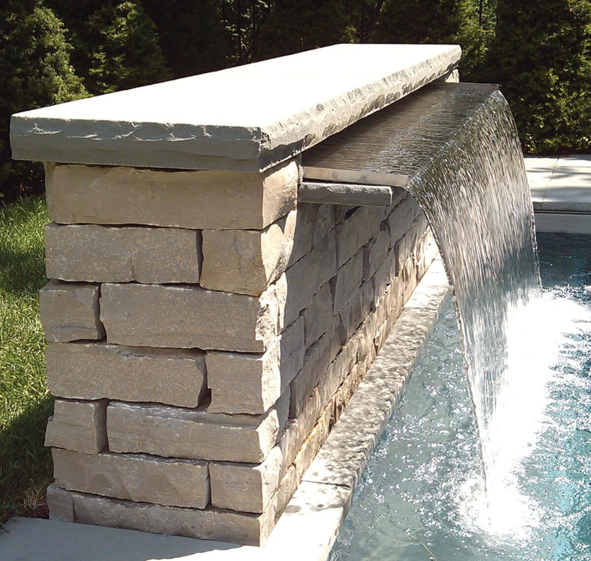 35 1/2 inch extended lip waterfall spillway installed in stone wall, wide sheet waterfall feature extending away from wall into pool