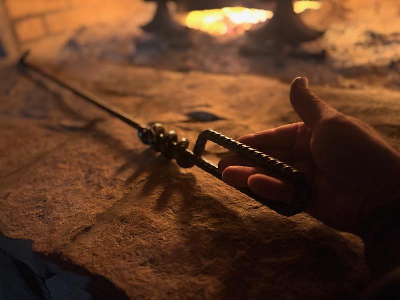 Good Works Hand Twisted Fire Poker in use by a cozy outdoor fire, demonstrating its effectiveness in managing firewood.