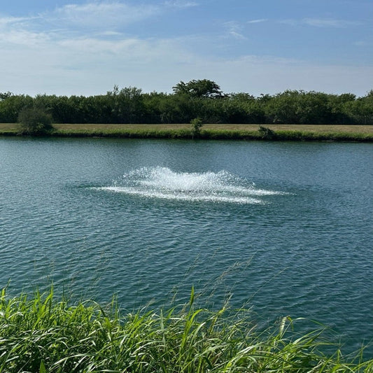 Aquarian Pro surface aerator running mid-pond on a sunny day with treeline in the background