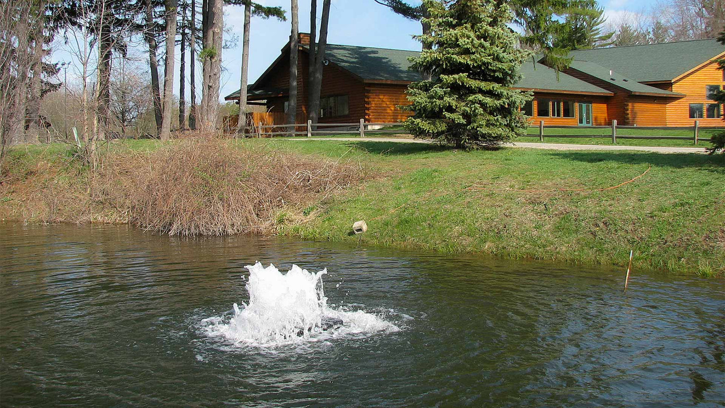solar powered pond aerator creating surface spray circulation in a residential pond near a cabin