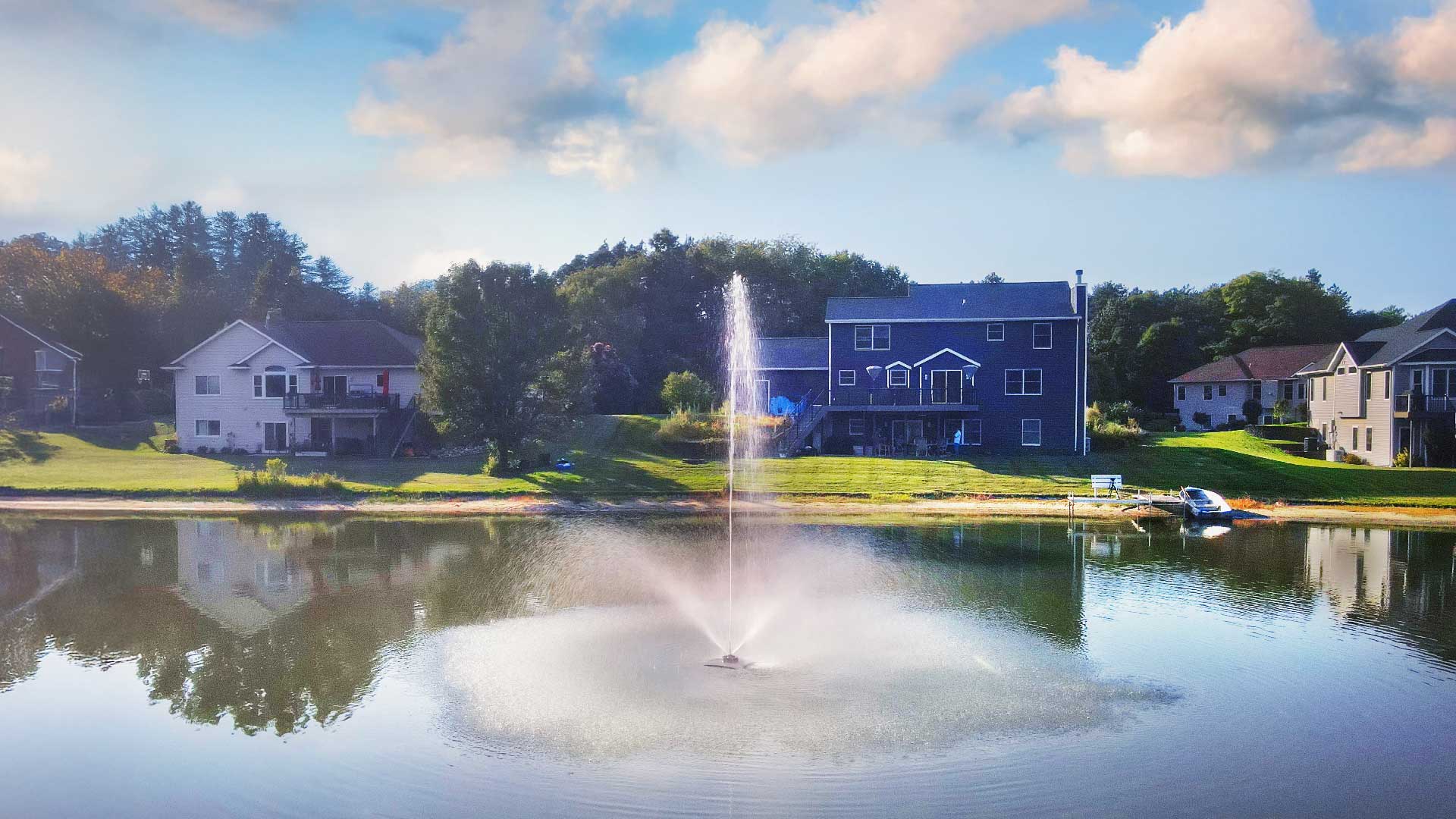 Scott Aerator Solar Skyward 1/2 HP solar pond fountain spraying tall display in residential lake with shoreline homes